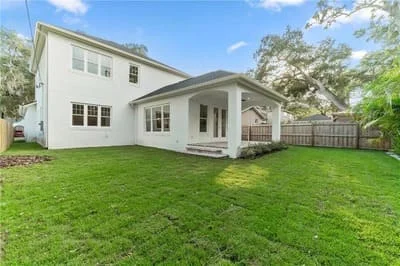 White farmhouse addition with covered porch, board-and-batten siding, and manicured lawn