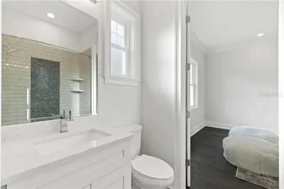 Modern bathroom with white vanity, subway tile wall, frameless glass shower, and dark flooring