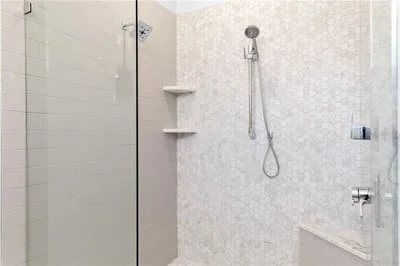 Walk-in shower with marble tile, frameless glass door, chrome fixtures, and built-in shelves